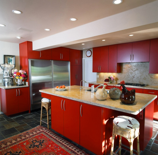 Bild på ett kök, med en dubbel diskho, släta luckor, röda skåp, beige stänkskydd, stänkskydd i sten, rostfria vitvaror och en köksö