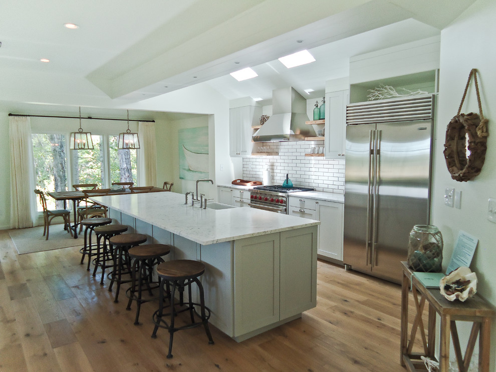 Inspiration for a mid-sized coastal galley light wood floor open concept kitchen remodel in Miami with a farmhouse sink, shaker cabinets, gray cabinets, marble countertops, white backsplash, ceramic backsplash, stainless steel appliances and an island