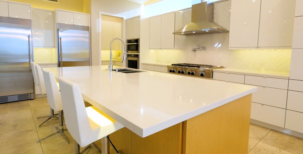 Exempel på ett stort modernt linjärt kök med öppen planlösning, med en nedsänkt diskho, släta luckor, vita skåp, vitt stänkskydd, stänkskydd i tunnelbanekakel, rostfria vitvaror, en köksö, laminatbänkskiva, travertin golv och beiget golv
