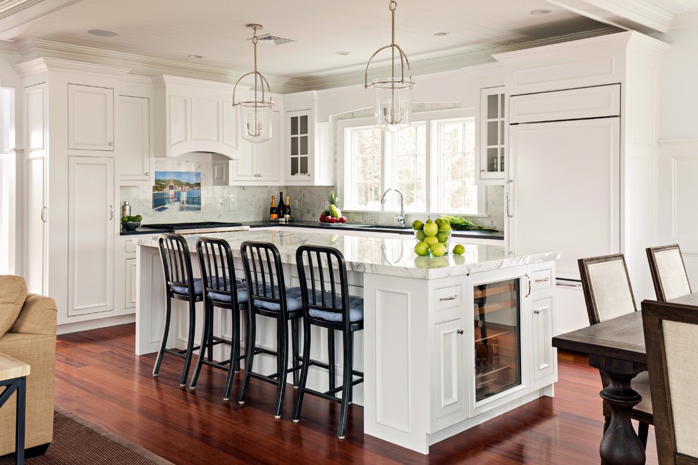 Klassisk inredning av ett mellanstort kök, med en undermonterad diskho, luckor med profilerade fronter, vita skåp, marmorbänkskiva, vitt stänkskydd, stänkskydd i stenkakel, integrerade vitvaror, mörkt trägolv och en köksö