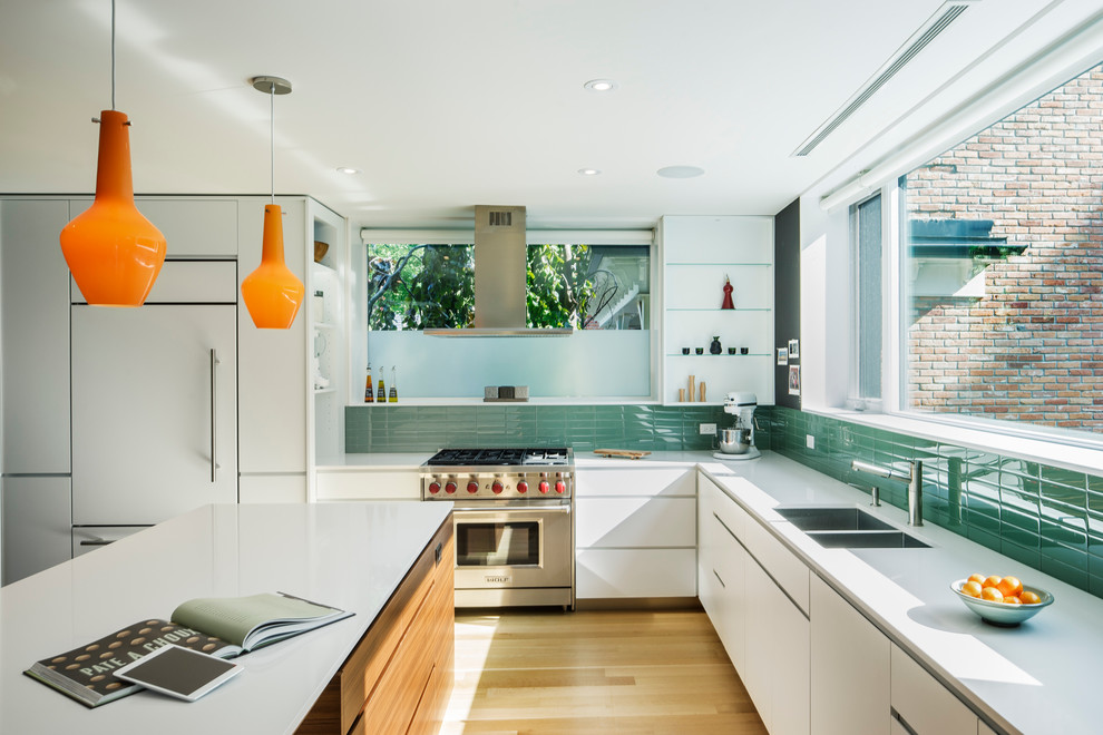 Small contemporary l-shaped open plan kitchen in Toronto with a submerged sink, flat-panel cabinets, white cabinets, green splashback, glass tiled splashback, integrated appliances, light hardwood flooring and an island.
