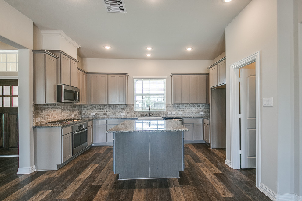 This is an example of a traditional u-shaped kitchen in Houston with a belfast sink, granite worktops, stainless steel appliances, an island and brown floors.
