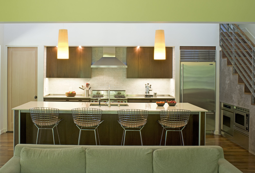 Свежая идея для дизайна: параллельная кухня-гостиная в современном стиле с техникой из нержавеющей стали, врезной мойкой, плоскими фасадами, фасадами цвета дерева среднего тона, белым фартуком и акцентной стеной - отличное фото интерьера