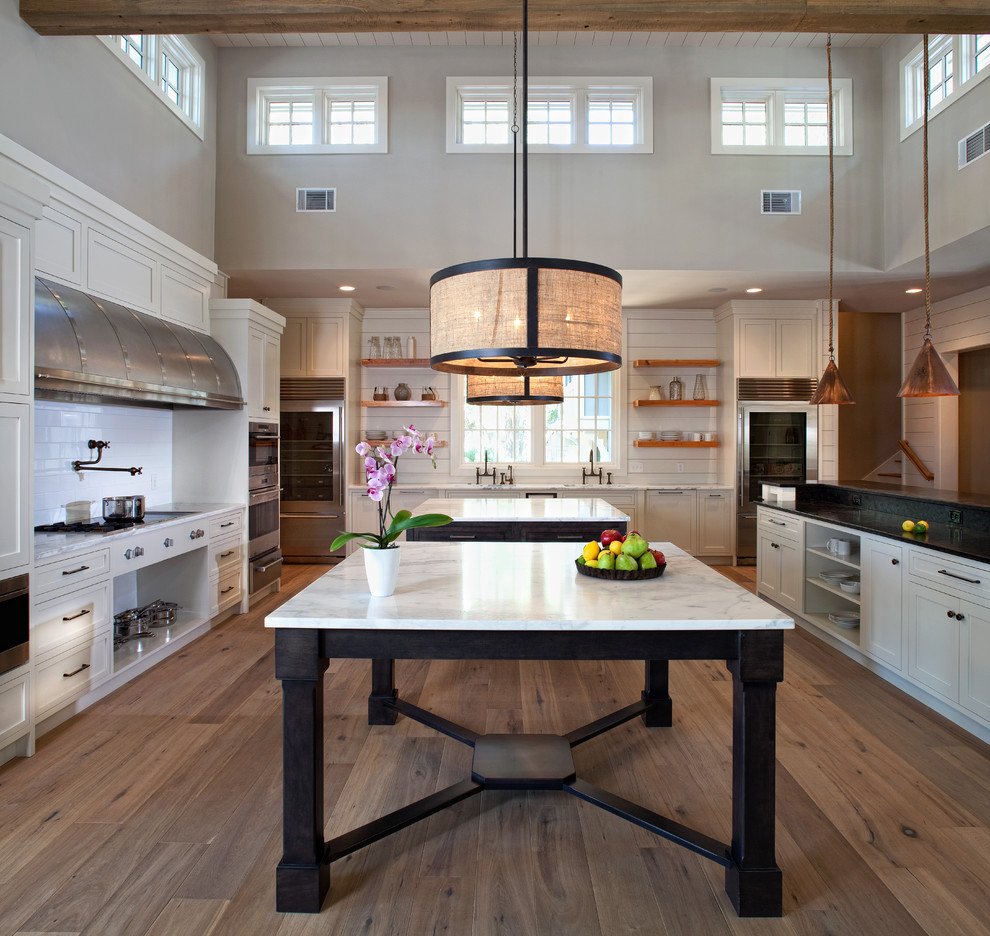 Geräumige Küche in U-Form mit Schrankfronten im Shaker-Stil, weißen Schränken, Küchenrückwand in Weiß, Küchengeräten aus Edelstahl, braunem Holzboden und zwei Kücheninseln in Charleston