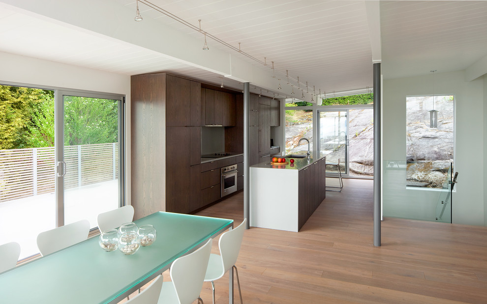 На фото: кухня в стиле модернизм с обеденным столом, врезной мойкой, плоскими фасадами, темными деревянными фасадами и техникой из нержавеющей стали