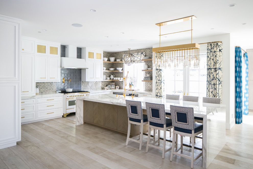 Photo of a coastal u-shaped kitchen in Orange County with beaded cabinets, white cabinets, beige splashback, white appliances, light hardwood flooring, an island and beige floors.