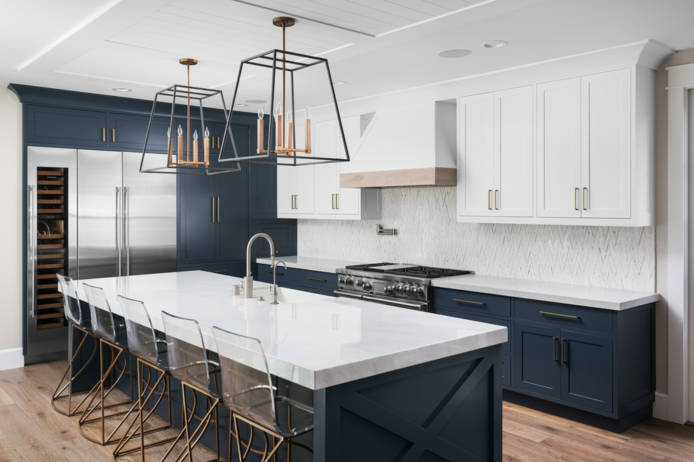 Klassische Küche in L-Form mit Landhausspüle, Schrankfronten im Shaker-Stil, blauen Schränken, Küchenrückwand in Weiß, Küchengeräten aus Edelstahl, braunem Holzboden, Kücheninsel, braunem Boden und weißer Arbeitsplatte in Orange County