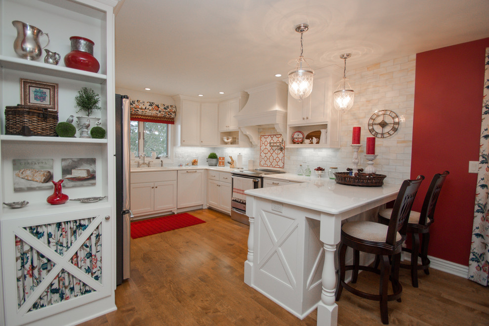 This is an example of a small classic u-shaped kitchen/diner in Milwaukee with recessed-panel cabinets, white cabinets, white splashback, ceramic splashback, medium hardwood flooring, stainless steel appliances and a breakfast bar.