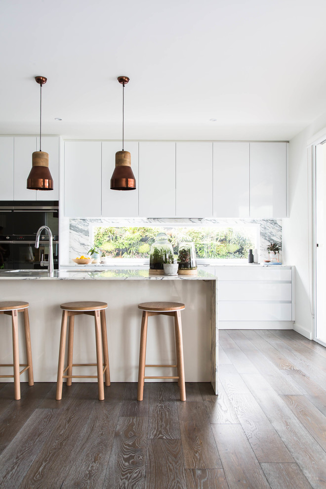 Design ideas for a scandi galley kitchen in Melbourne with flat-panel cabinets, white cabinets, window splashback, dark hardwood flooring, an island, brown floors, marble worktops, black appliances and white worktops.