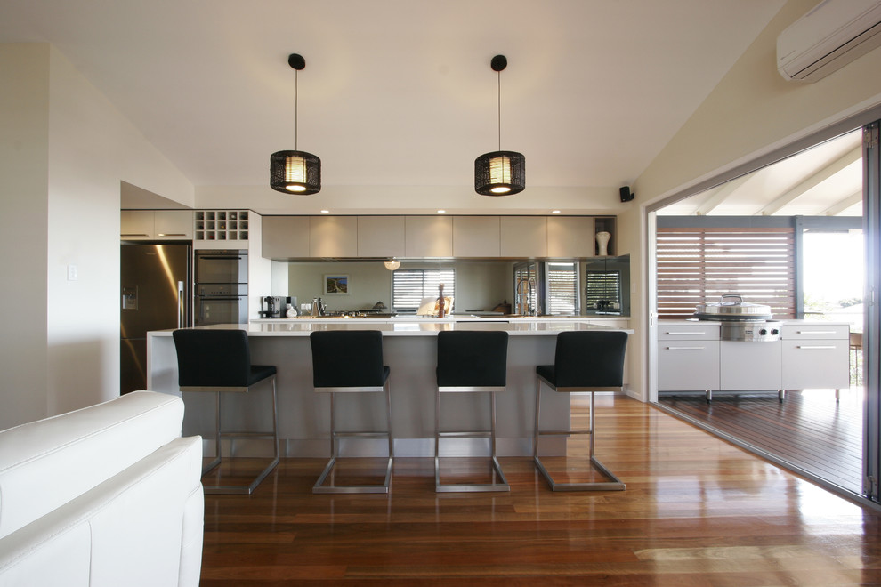 Inspiration for a medium sized contemporary single-wall kitchen/diner in Brisbane with stainless steel appliances, a built-in sink, flat-panel cabinets, beige cabinets, engineered stone countertops, green splashback, medium hardwood flooring and an island.