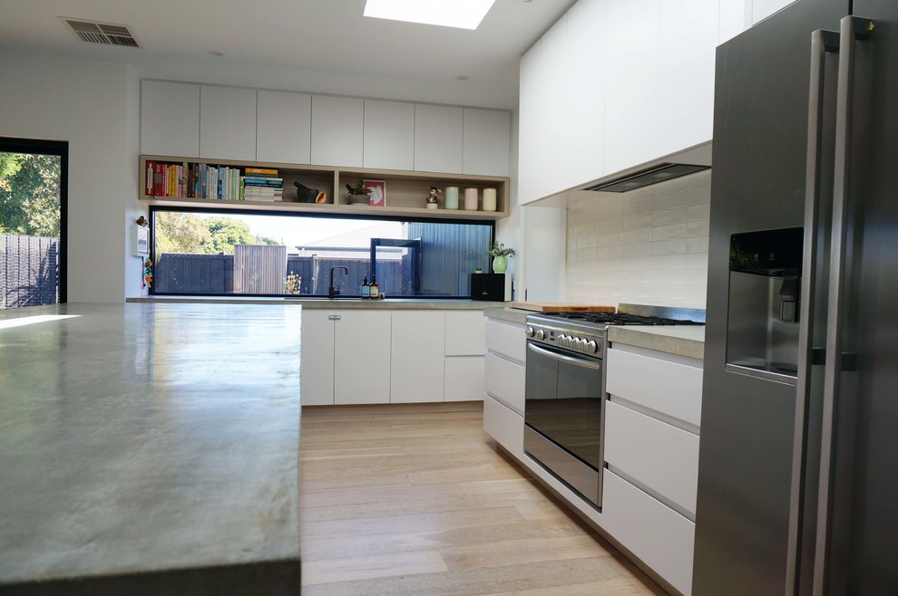 Aménagement d'une cuisine ouverte moderne avec un placard à porte plane, des portes de placard blanches, un plan de travail en béton, une crédence blanche et îlot.