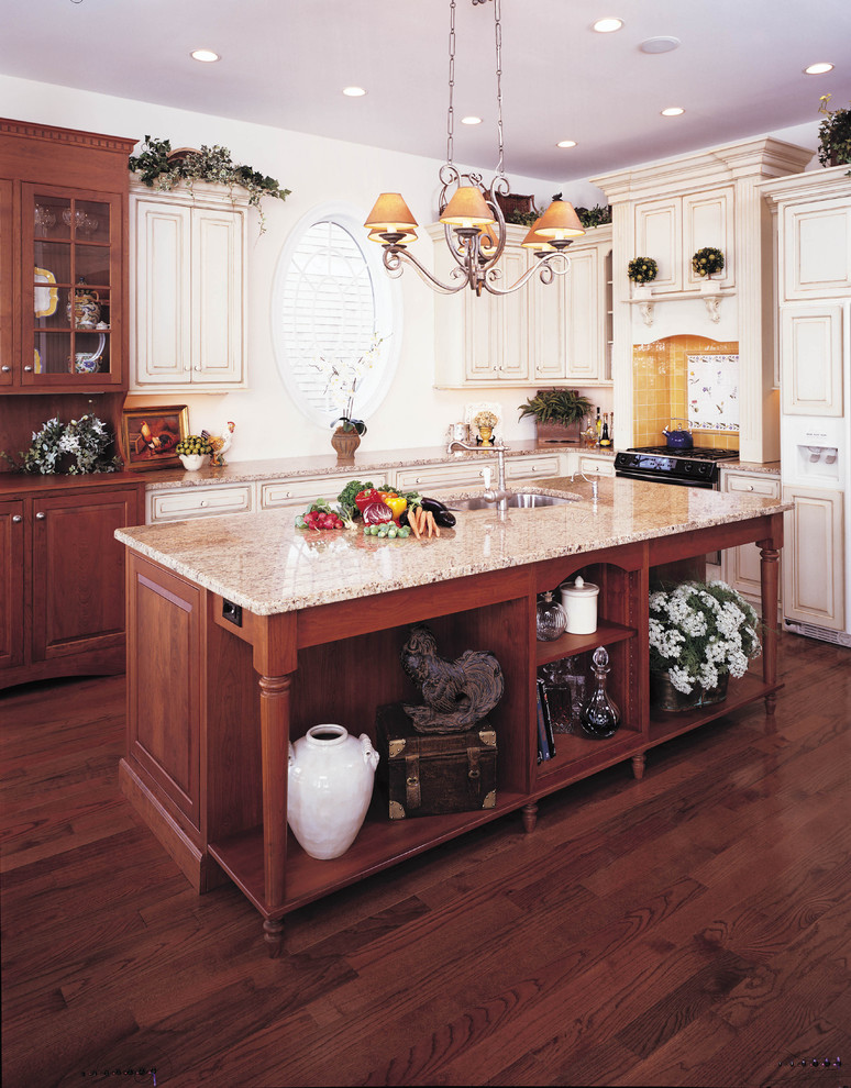 Inredning av ett klassiskt avskilt, stort brun brunt l-kök, med granitbänkskiva, en undermonterad diskho, luckor med upphöjd panel, skåp i ljust trä, gult stänkskydd, stänkskydd i porslinskakel, mörkt trägolv, en köksö och brunt golv