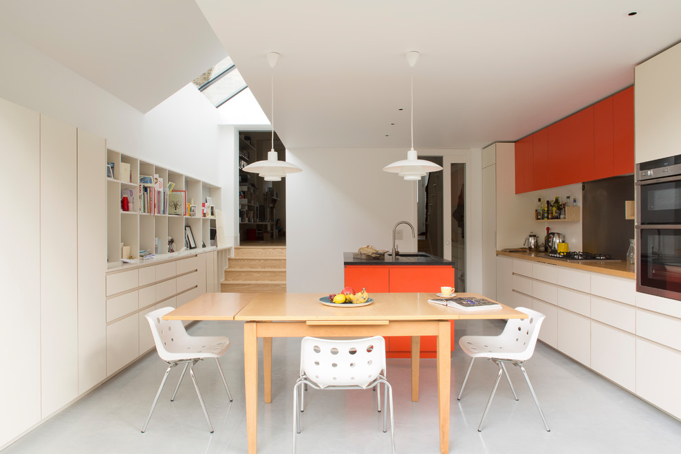 Идея дизайна: параллельная кухня среднего размера с обеденным столом, врезной мойкой, плоскими фасадами, оранжевыми фасадами, серым фартуком, техникой под мебельный фасад, бетонным полом, островом и серым полом