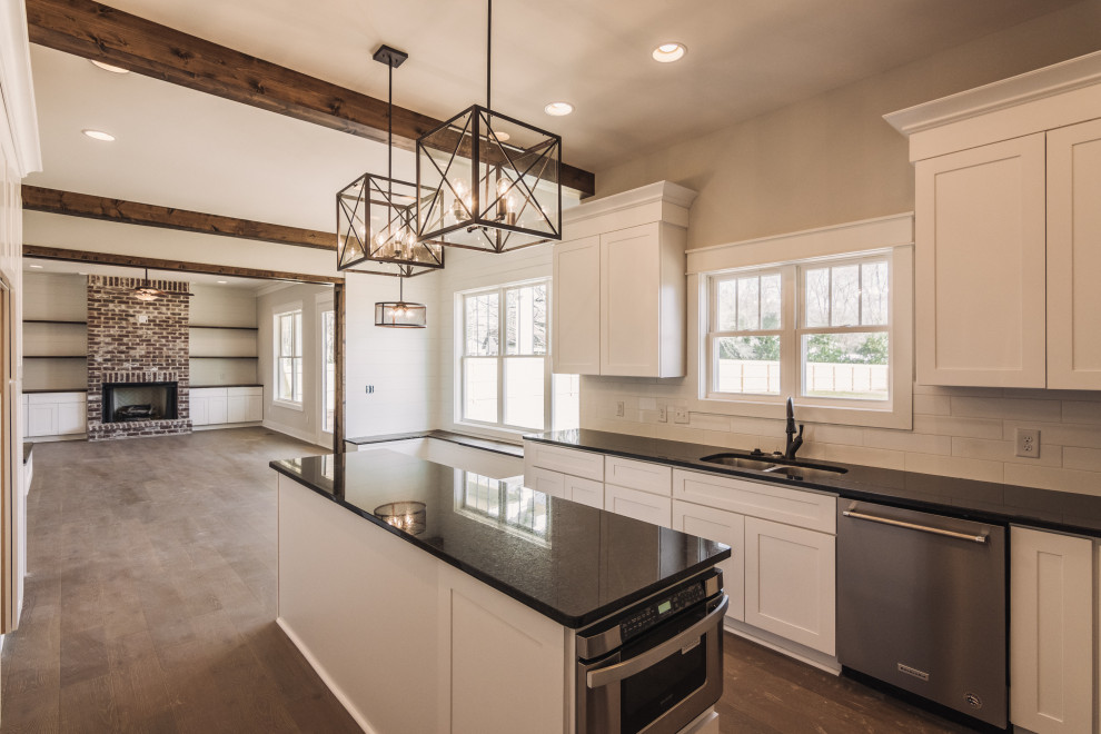 Medium sized traditional u-shaped kitchen/diner in Nashville with a submerged sink, recessed-panel cabinets, white cabinets, engineered stone countertops, white splashback, stone tiled splashback, stainless steel appliances, dark hardwood flooring, an island, brown floors and black worktops.