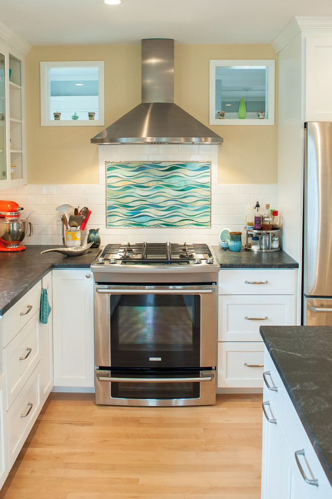 Klassisk inredning av ett kök, med luckor med infälld panel, vita skåp, flerfärgad stänkskydd och rostfria vitvaror