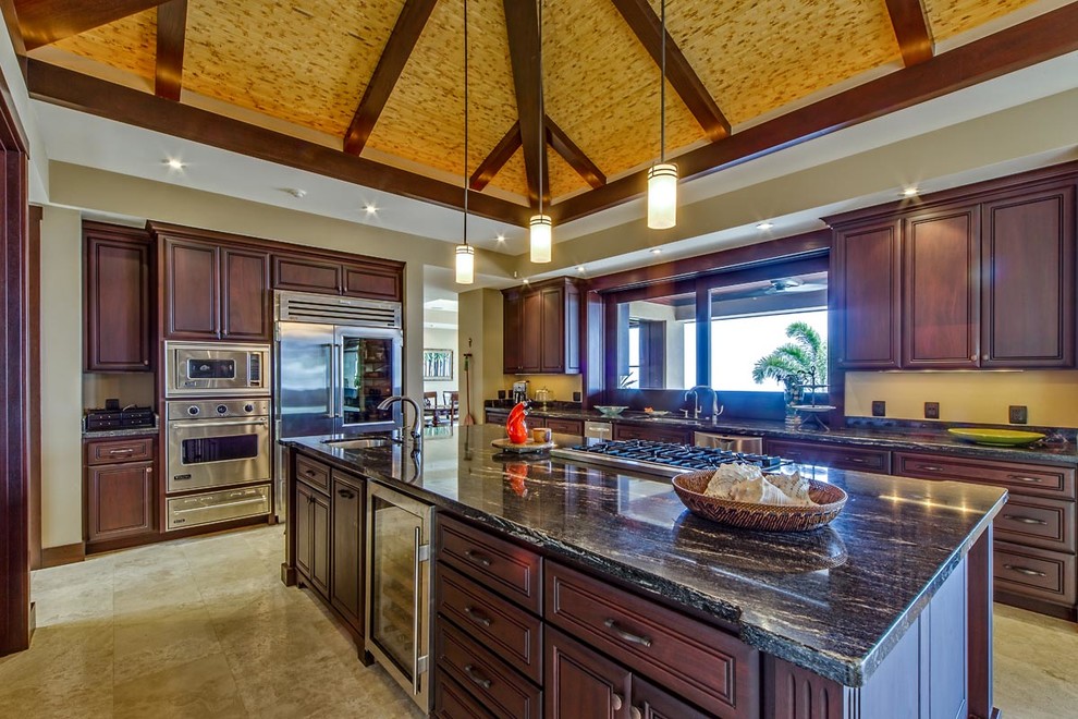 Large island style u-shaped travertine floor open concept kitchen photo in Hawaii with an undermount sink, raised-panel cabinets, brown cabinets, granite countertops, black backsplash, stone slab backsplash, stainless steel appliances and an island