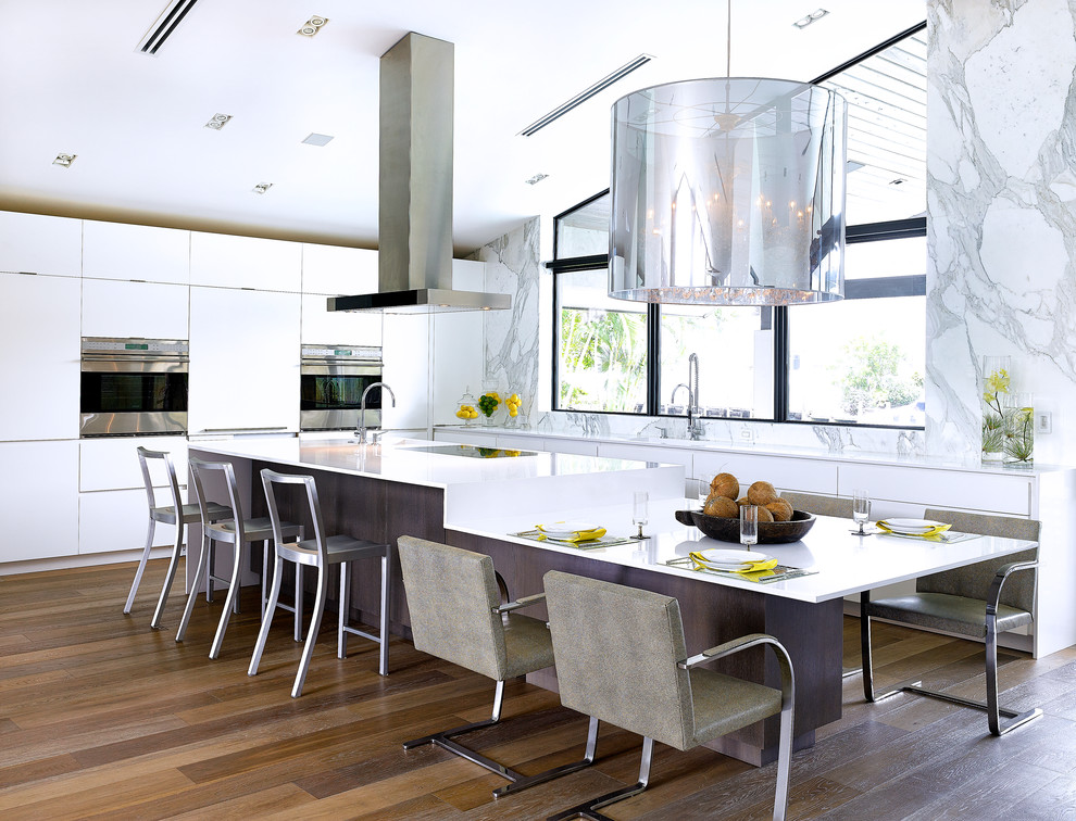 Photo of a contemporary l-shaped kitchen/diner in Miami with flat-panel cabinets, white cabinets, white splashback, stone slab splashback, stainless steel appliances, an island and dark hardwood flooring.