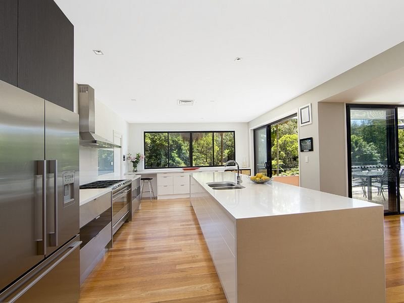 Large contemporary galley kitchen pantry in Sydney with a submerged sink, flat-panel cabinets, white cabinets, engineered stone countertops, white splashback, glass sheet splashback, stainless steel appliances, light hardwood flooring and multiple islands.