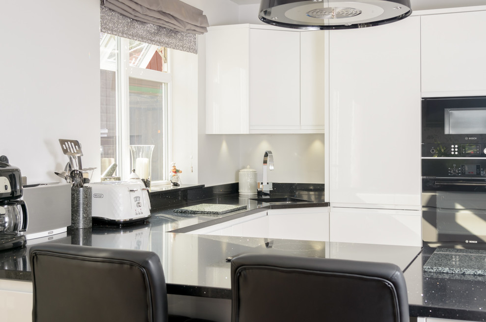 Kleine Moderne Wohnküche in U-Form mit weißen Schränken, Mineralwerkstoff-Arbeitsplatte und schwarzen Elektrogeräten in Sonstige