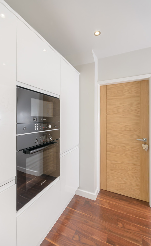 Modelo de cocina contemporánea pequeña con puertas de armario blancas, encimera de acrílico y electrodomésticos negros