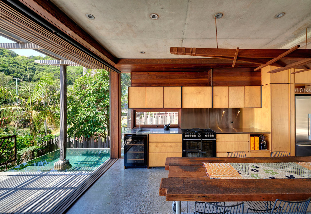 Foto på ett tropiskt grå linjärt kök och matrum, med släta luckor, skåp i mellenmörkt trä, svarta vitvaror, betonggolv och grått golv