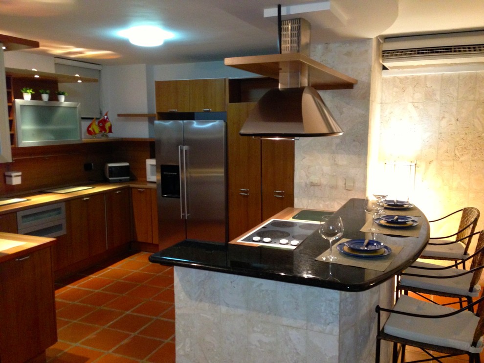 This is an example of a small beach style l-shaped open plan kitchen in Miami with flat-panel cabinets, dark wood cabinets, wood worktops, brown splashback, wood splashback, stainless steel appliances, terracotta flooring, an island and red floors.
