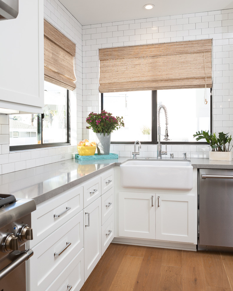 Bild på ett maritimt kök, med en rustik diskho, skåp i shakerstil, gröna skåp, bänkskiva i kvartsit, vitt stänkskydd, stänkskydd i tunnelbanekakel, rostfria vitvaror, mellanmörkt trägolv och en köksö
