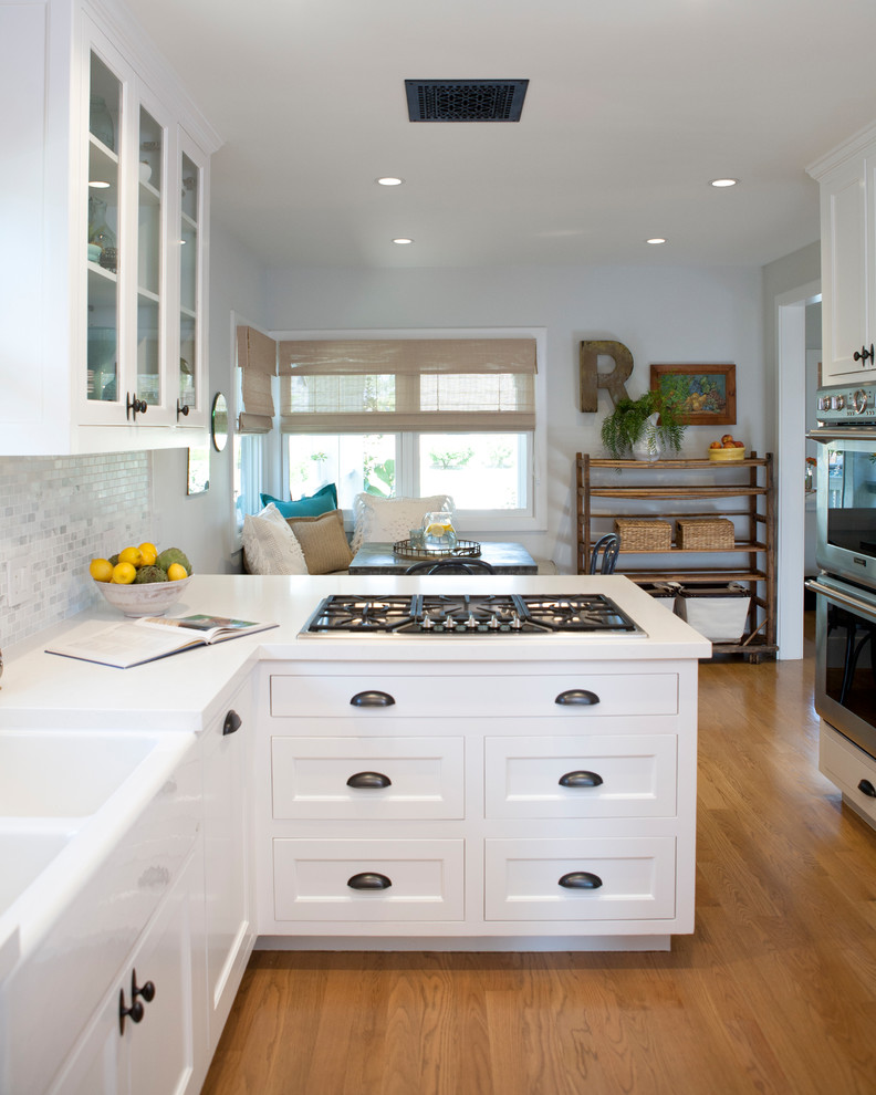 Maritime Wohnküche mit Küchenrückwand in Weiß, Küchengeräten aus Edelstahl, braunem Holzboden, Kücheninsel, braunem Boden und weißer Arbeitsplatte in Orange County