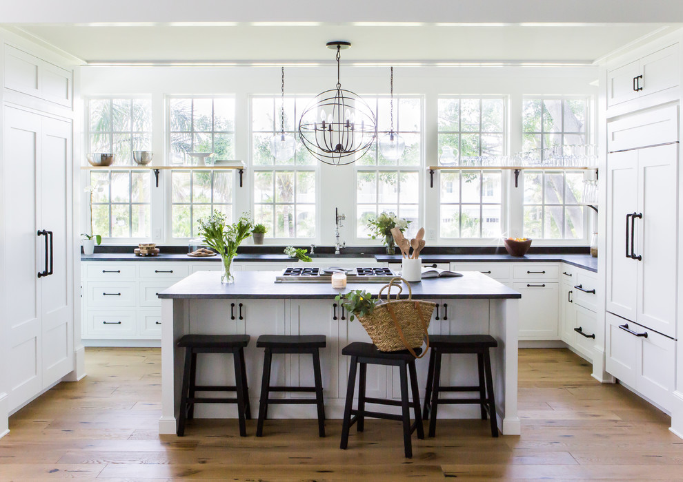 Inspiration for a coastal u-shaped medium tone wood floor and brown floor kitchen remodel in Tampa with a farmhouse sink, shaker cabinets, paneled appliances, an island and black countertops