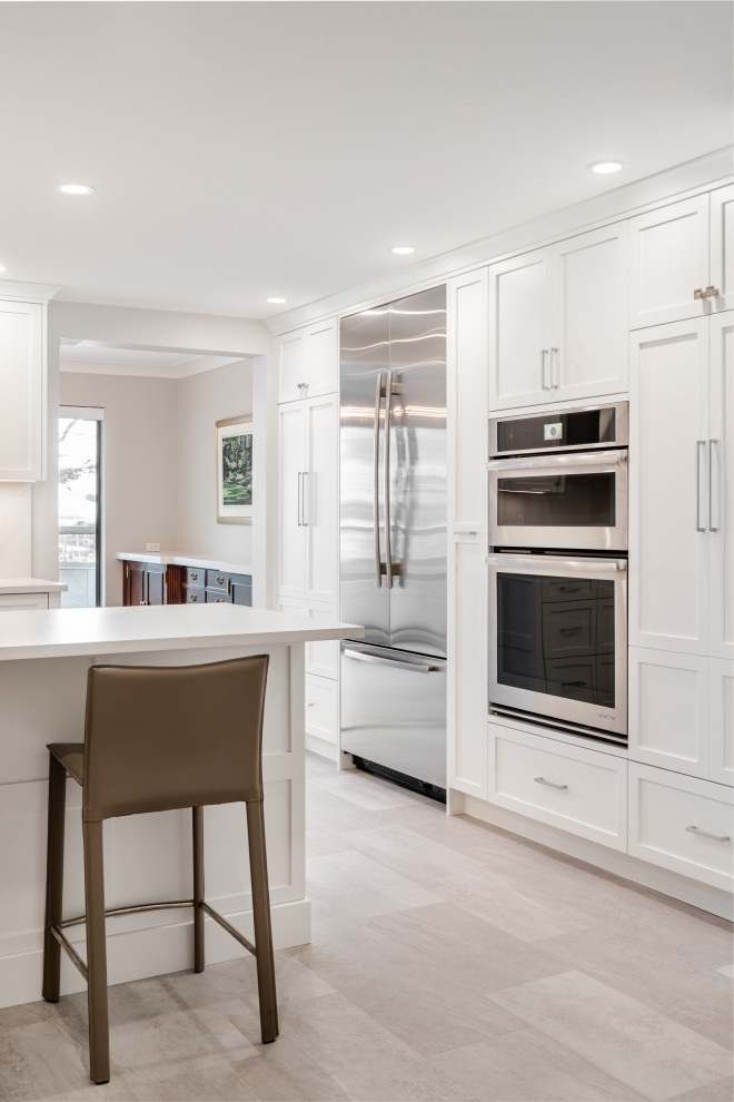 Small traditional u-shaped kitchen/diner in Vancouver with a submerged sink, shaker cabinets, white cabinets, engineered stone countertops, white splashback, stone slab splashback, stainless steel appliances, light hardwood flooring, a breakfast bar, white floors and white worktops.