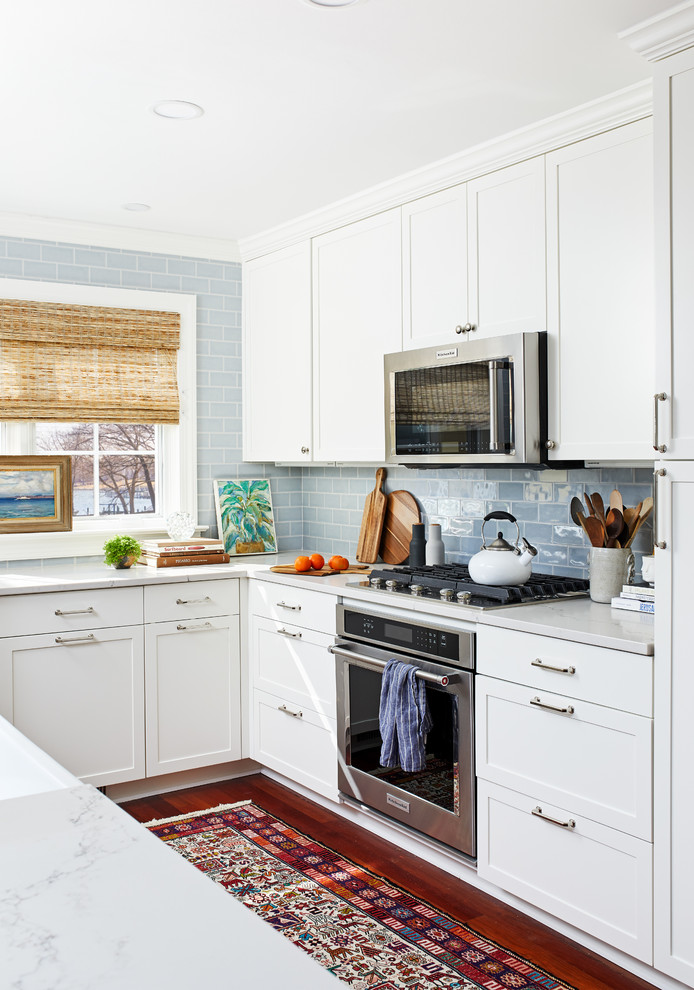 Example of a mid-sized transitional galley dark wood floor and brown floor enclosed kitchen design in Baltimore with a farmhouse sink, shaker cabinets, white cabinets, quartz countertops, blue backsplash, ceramic backsplash and stainless steel appliances