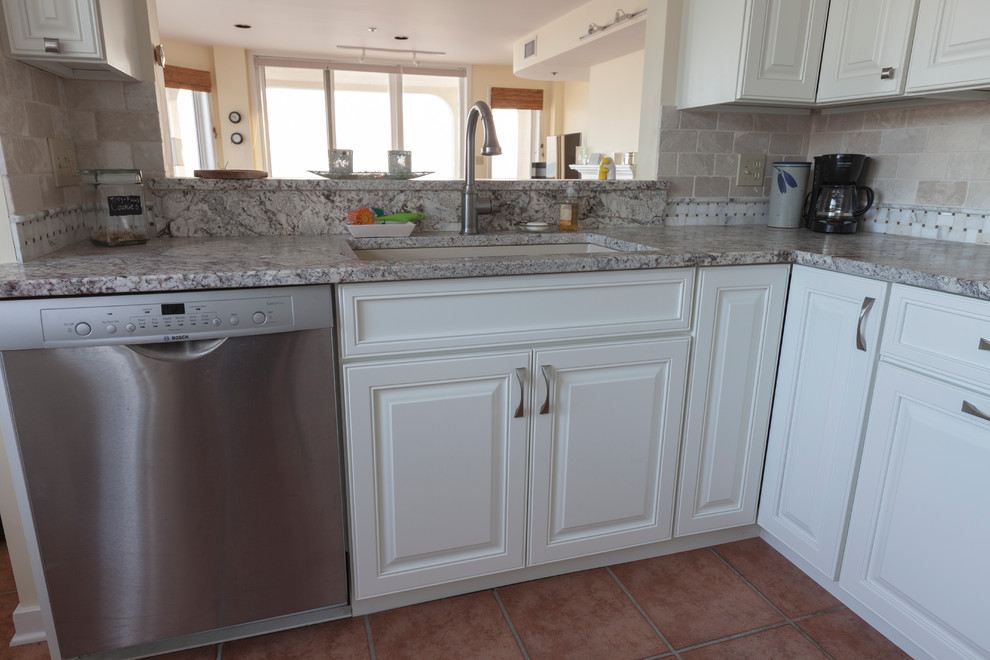 Klassisk inredning av ett avskilt, mellanstort u-kök, med en undermonterad diskho, luckor med upphöjd panel, vita skåp, granitbänkskiva, beige stänkskydd, stänkskydd i stenkakel och rostfria vitvaror