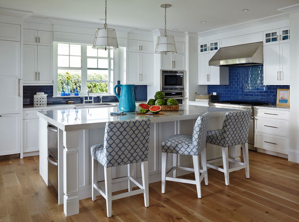 Foto på ett mellanstort maritimt kök, med blått stänkskydd, rostfria vitvaror, mellanmörkt trägolv, vita skåp, skåp i shakerstil, stänkskydd i tunnelbanekakel och en köksö