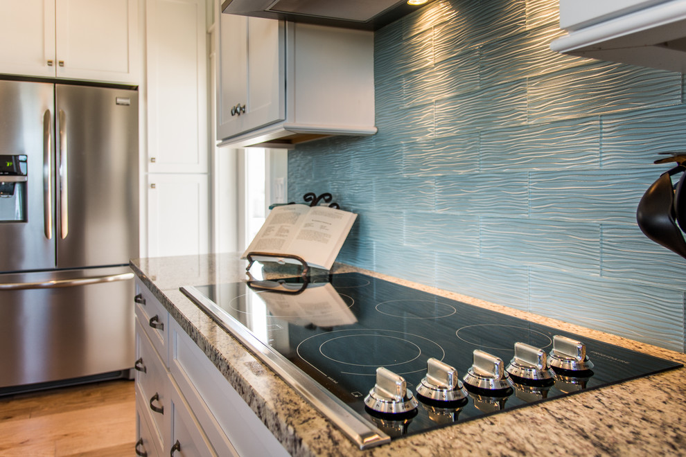 Maritim inredning av ett mellanstort kök, med en rustik diskho, skåp i shakerstil, vita skåp, bänkskiva i glas, blått stänkskydd, stänkskydd i keramik, rostfria vitvaror, mellanmörkt trägolv och en köksö