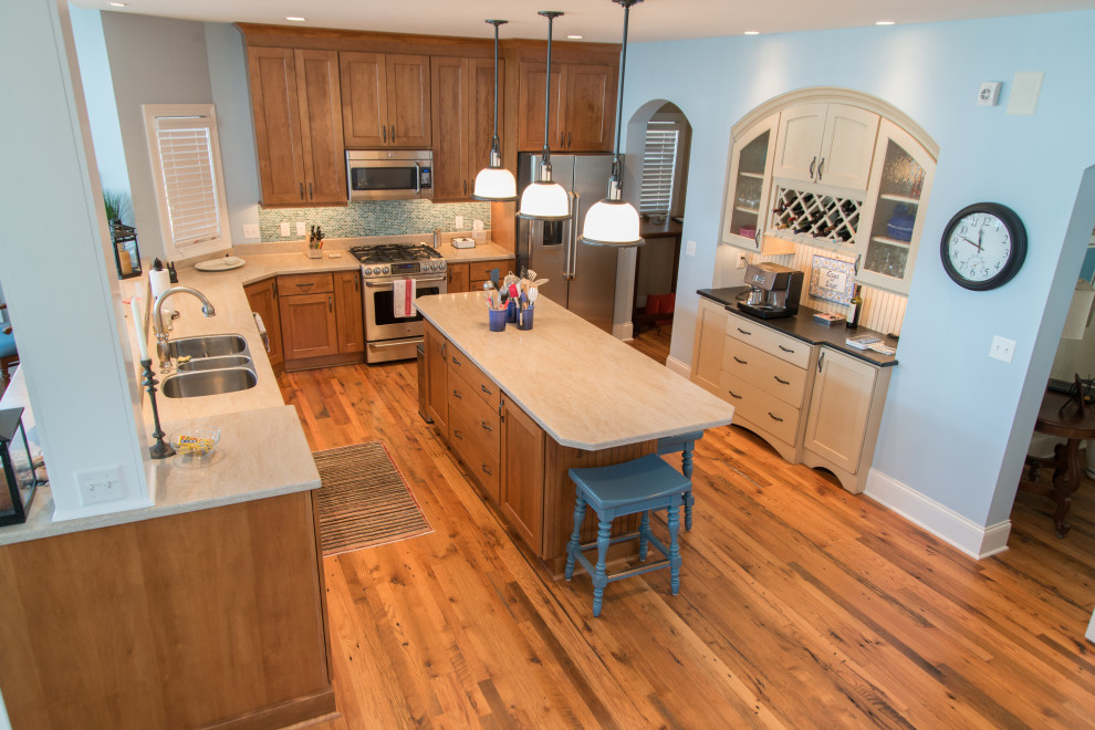 Inspiration for a large coastal l-shaped medium tone wood floor and brown floor eat-in kitchen remodel in Chicago with a triple-bowl sink, shaker cabinets, medium tone wood cabinets, quartzite countertops, blue backsplash, glass tile backsplash, stainless steel appliances, an island and beige countertops