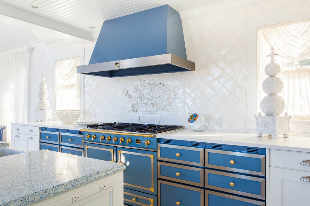 Modelo de cocina costera con armarios estilo shaker, puertas de armario azules, salpicadero blanco, salpicadero de azulejos de porcelana, electrodomésticos de colores y una isla