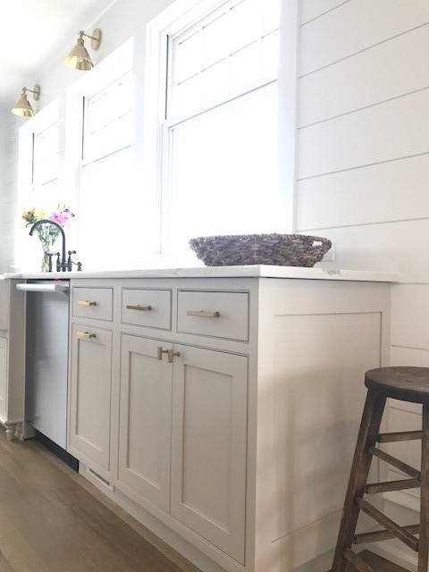 This is an example of a large farmhouse l-shaped kitchen/diner in Philadelphia with a belfast sink, beaded cabinets, grey cabinets, quartz worktops, white splashback, ceramic splashback, stainless steel appliances, medium hardwood flooring, an island and orange floors.