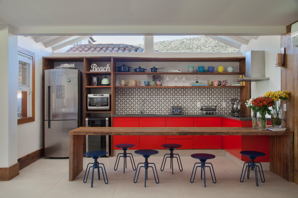 Exemple d'une cuisine bord de mer en L avec un placard à porte plane, des portes de placard rouges, une crédence multicolore, un électroménager en acier inoxydable, une péninsule et un sol beige.