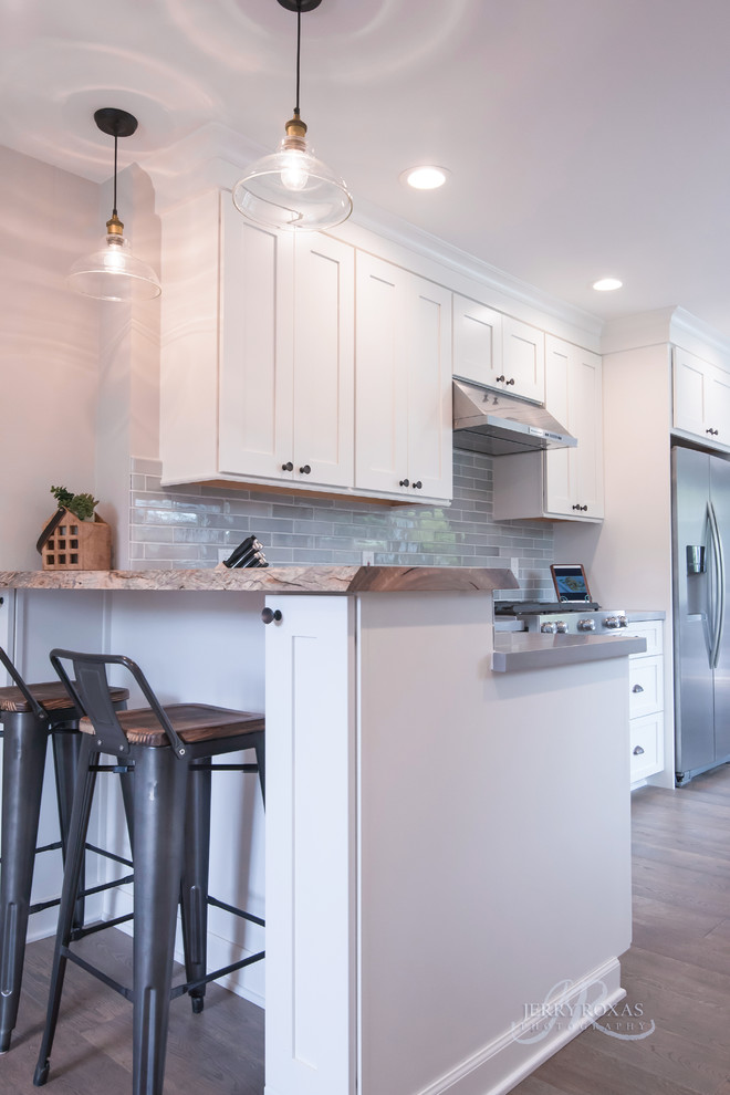 Example of a mid-sized beach style l-shaped dark wood floor and brown floor eat-in kitchen design in San Diego with shaker cabinets, white cabinets, solid surface countertops, gray backsplash, porcelain backsplash, stainless steel appliances and an island