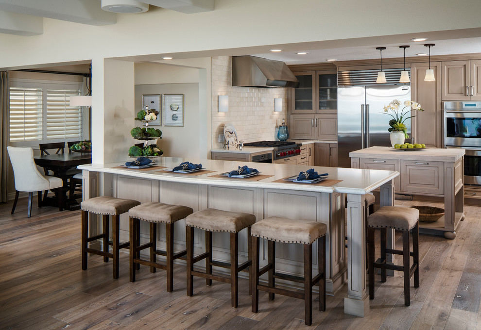 Design ideas for a traditional kitchen/diner in Orange County with raised-panel cabinets, engineered stone countertops, beige splashback, metro tiled splashback, stainless steel appliances, an island, light wood cabinets and medium hardwood flooring.