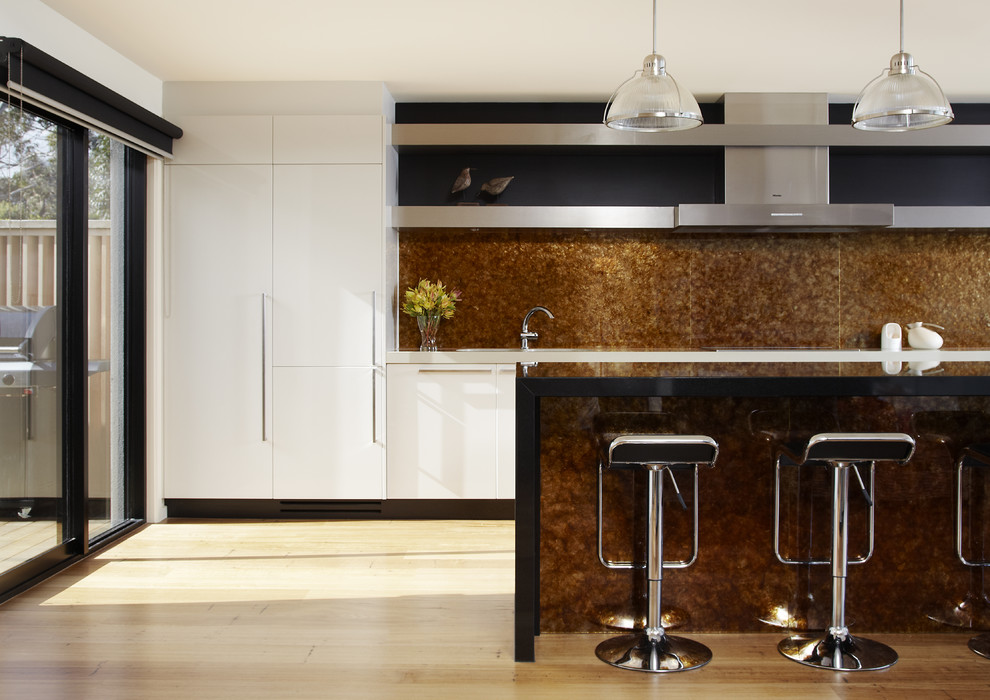 Example of a mid-sized beach style single-wall light wood floor eat-in kitchen design in Melbourne with flat-panel cabinets, white cabinets, brown backsplash, granite countertops, stone slab backsplash, stainless steel appliances and an island