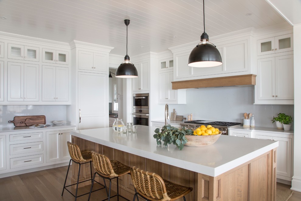 Foto di una cucina stile marinaro con ante in stile shaker, ante bianche, paraspruzzi bianco, elettrodomestici da incasso, pavimento in legno massello medio, pavimento marrone e top bianco