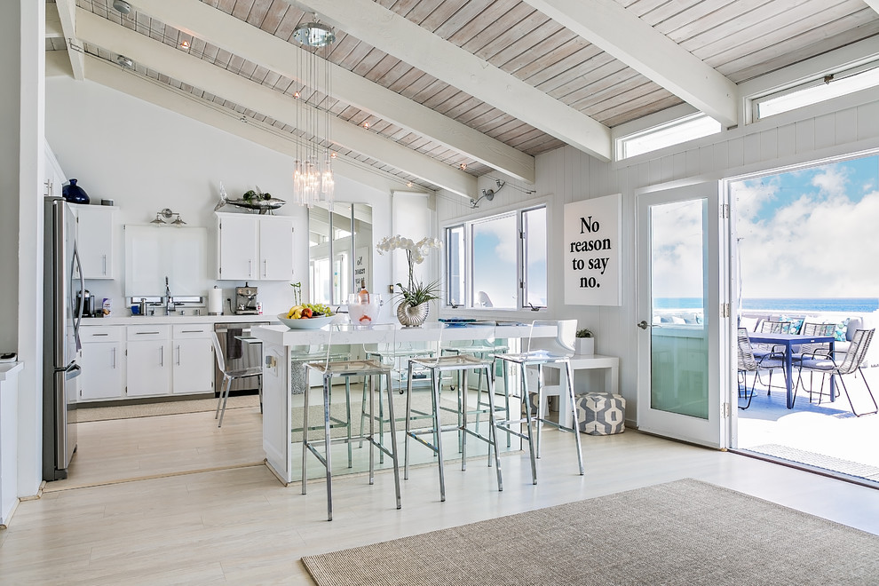 Inspiration for a medium sized coastal l-shaped open plan kitchen in Los Angeles with white cabinets, marble worktops, white splashback, stainless steel appliances, light hardwood flooring and an island.