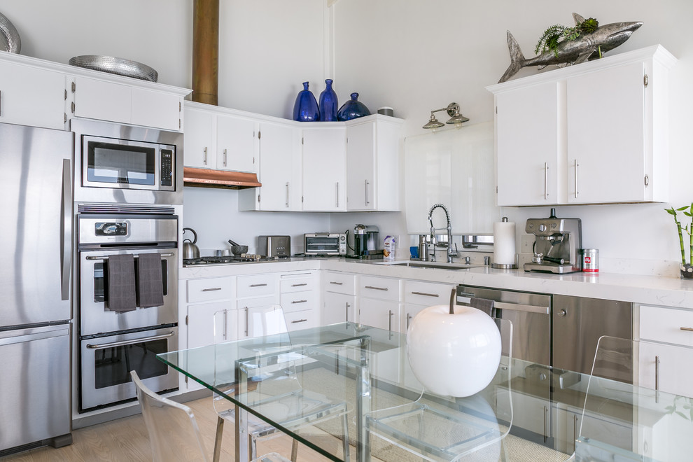 Example of a small beach style l-shaped light wood floor open concept kitchen design in Los Angeles with flat-panel cabinets, white cabinets, marble countertops, white backsplash, stainless steel appliances and an island