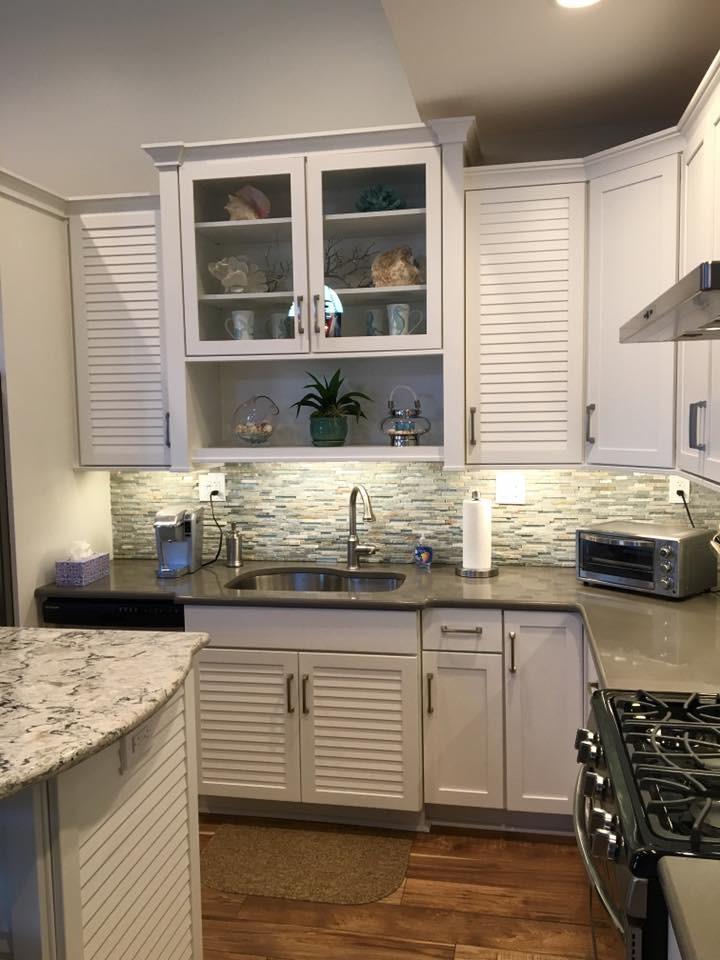 Mid-sized beach style l-shaped medium tone wood floor open concept kitchen photo in New York with an undermount sink, recessed-panel cabinets, white cabinets, laminate countertops, gray backsplash, matchstick tile backsplash, stainless steel appliances and an island