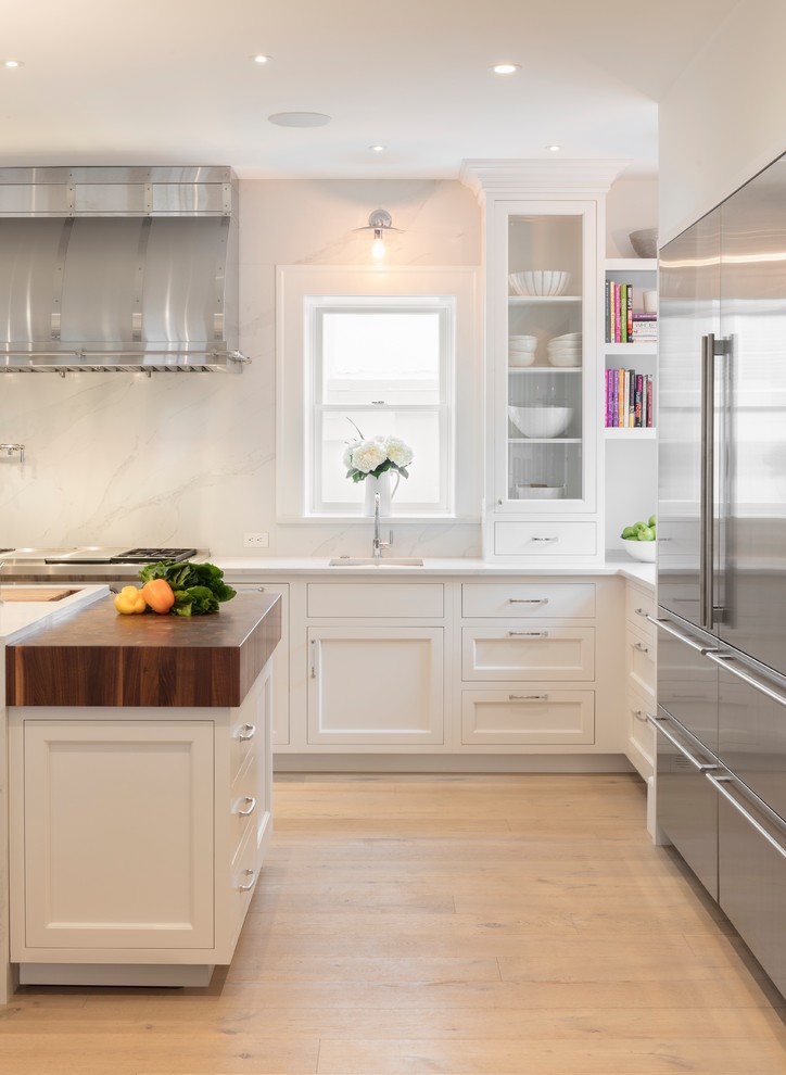 Exempel på ett stort klassiskt vit vitt kök och matrum, med en undermonterad diskho, vita skåp, bänkskiva i kvarts, vitt stänkskydd, rostfria vitvaror, ljust trägolv, en köksö och luckor med infälld panel