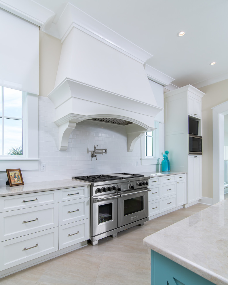 Bild på ett stort maritimt kök, med en undermonterad diskho, luckor med profilerade fronter, vita skåp, granitbänkskiva, vitt stänkskydd, stänkskydd i porslinskakel, integrerade vitvaror och en köksö