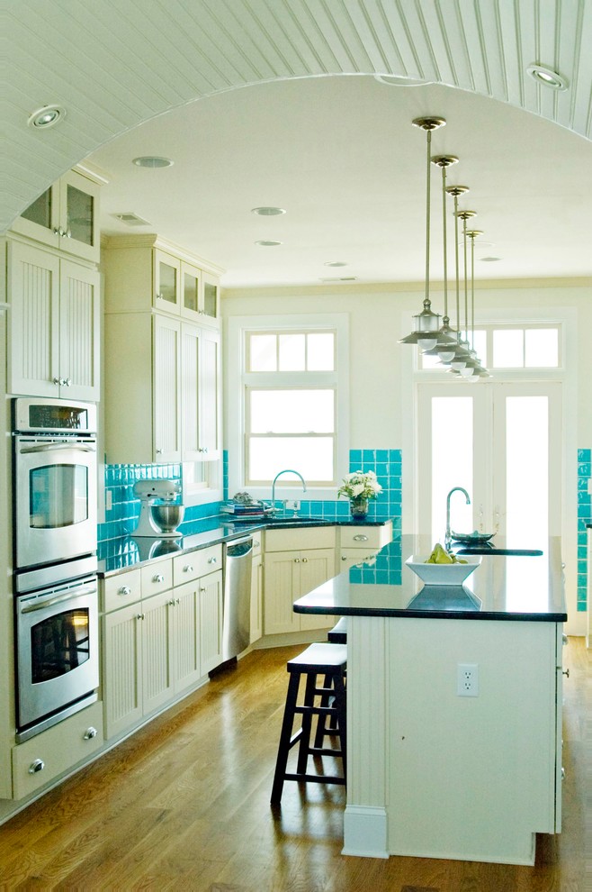 Maritime Küche mit Unterbauwaschbecken, Kassettenfronten, weißen Schränken, Küchenrückwand in Blau, Küchengeräten aus Edelstahl und braunem Holzboden in Wilmington