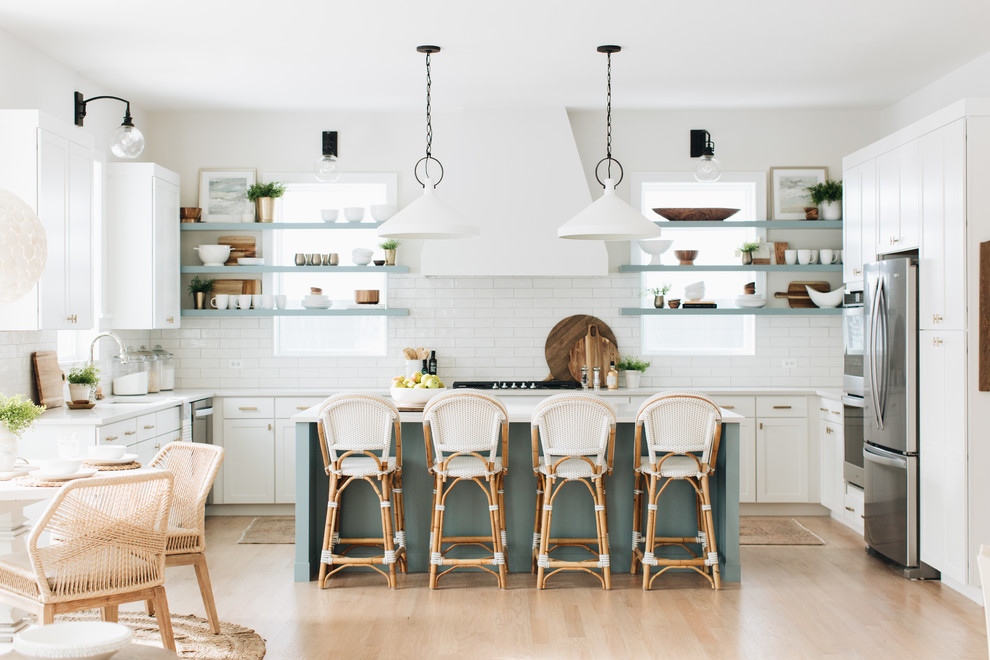 Design ideas for a nautical u-shaped kitchen in Chicago with a submerged sink, shaker cabinets, white cabinets, white splashback, metro tiled splashback, stainless steel appliances, light hardwood flooring, an island, beige floors and white worktops.