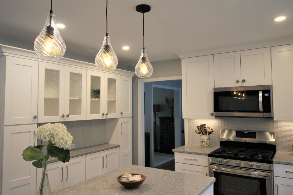 Example of a mid-sized beach style l-shaped vinyl floor and multicolored floor eat-in kitchen design in Burlington with an undermount sink, shaker cabinets, white cabinets, quartz countertops, gray backsplash, glass tile backsplash, stainless steel appliances, an island and gray countertops
